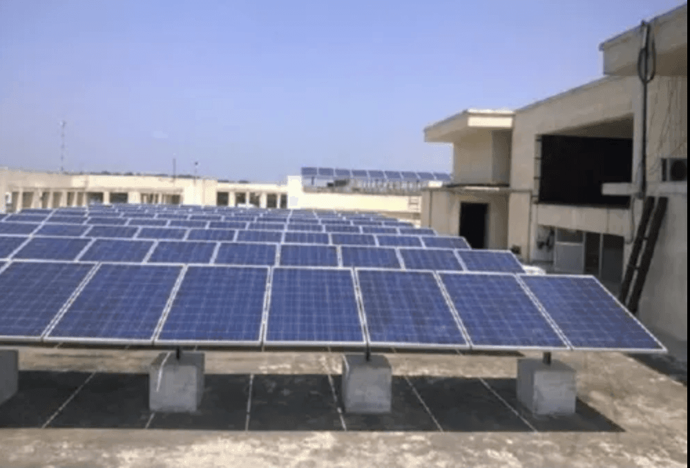 Array of solar panels mounted on a concrete rooftop under a clear blue sky.