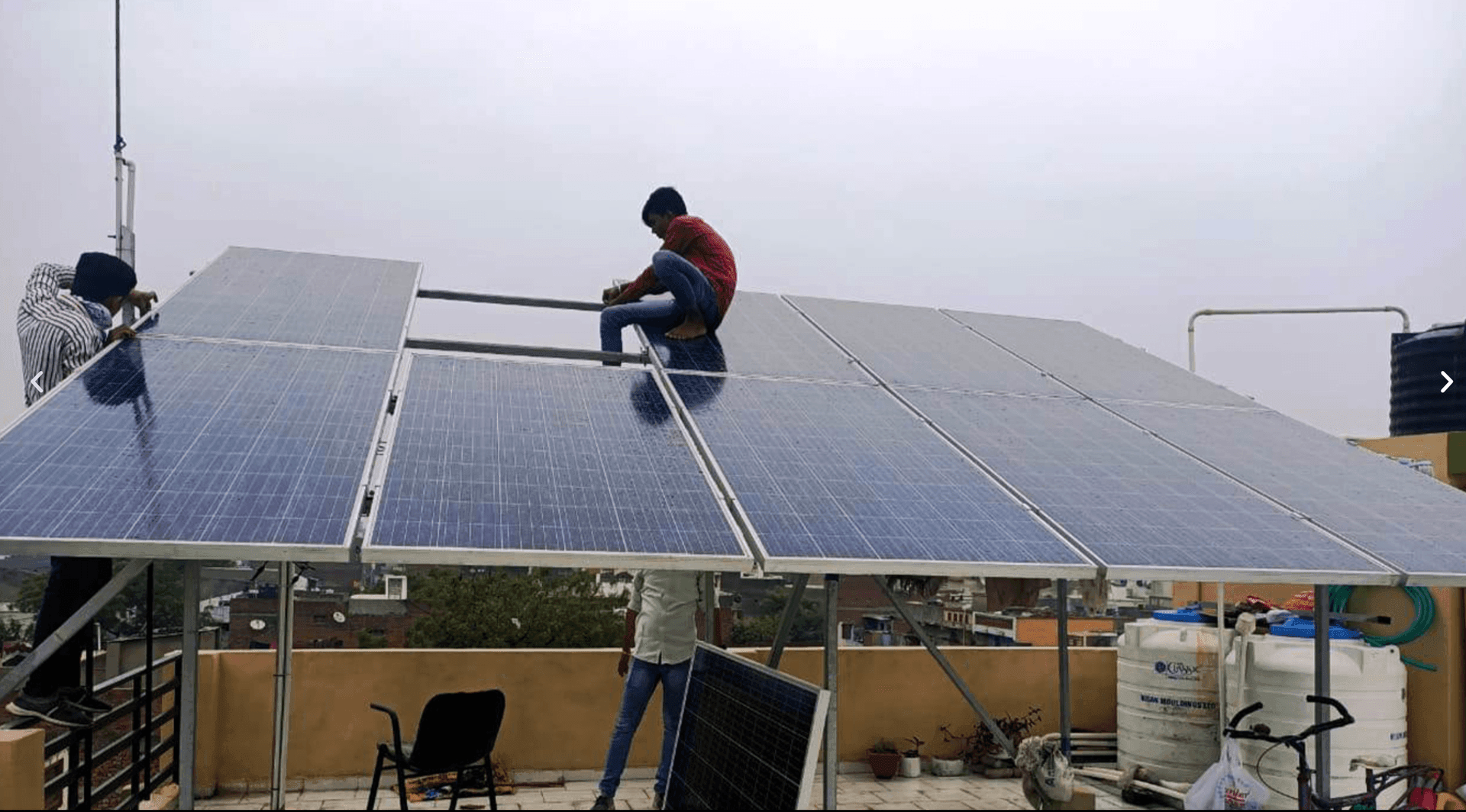 Workers installing solar panels on a rooftop with buildings in the background.