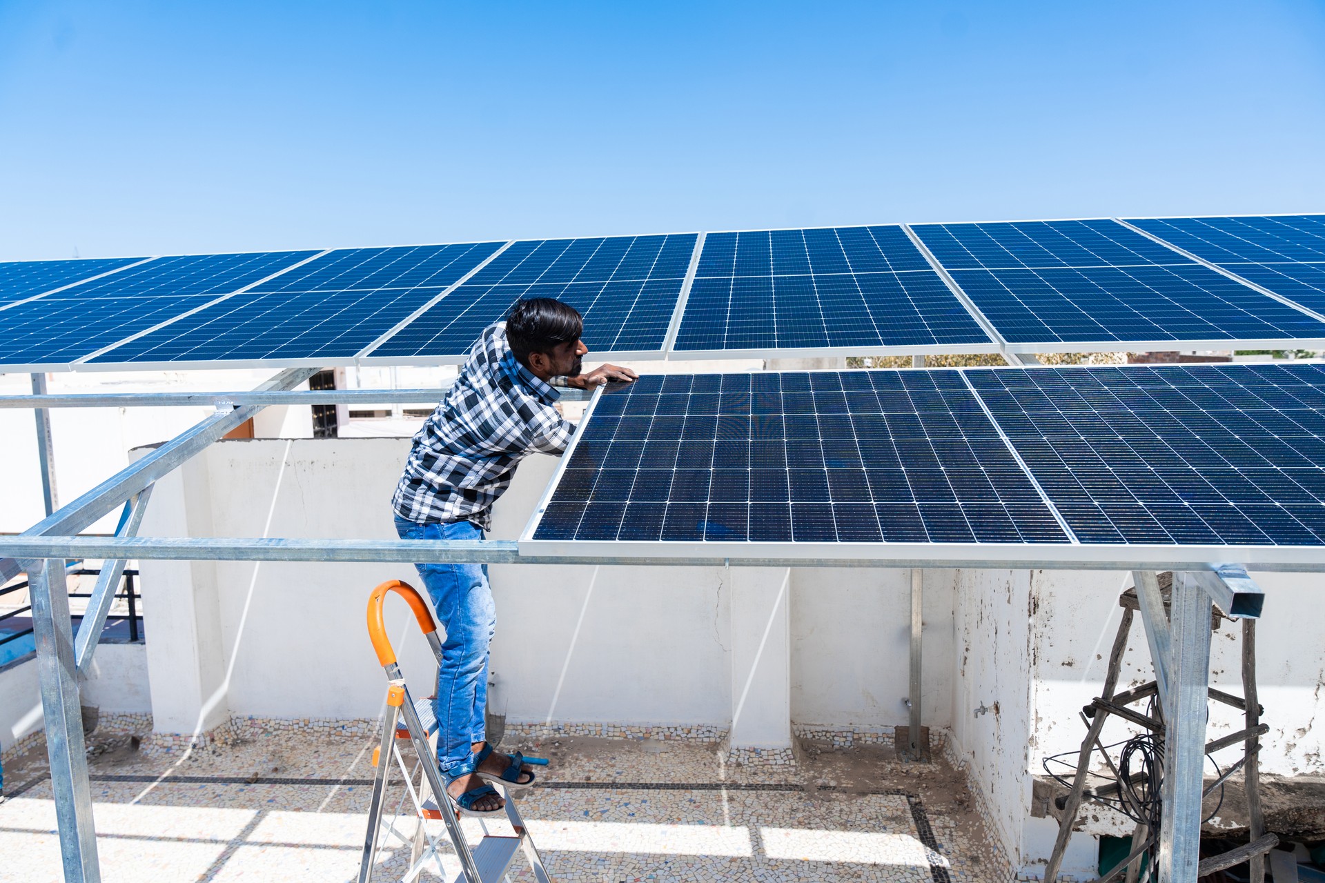 Indian worker installing solar panels on roof of house. Maintenance of photovoltaic panel system. Concept of alternative, renewable energy.